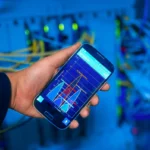 Tangan memegang smartphone menampilkan analisis jaringan di lingkungan server teknologi tinggi